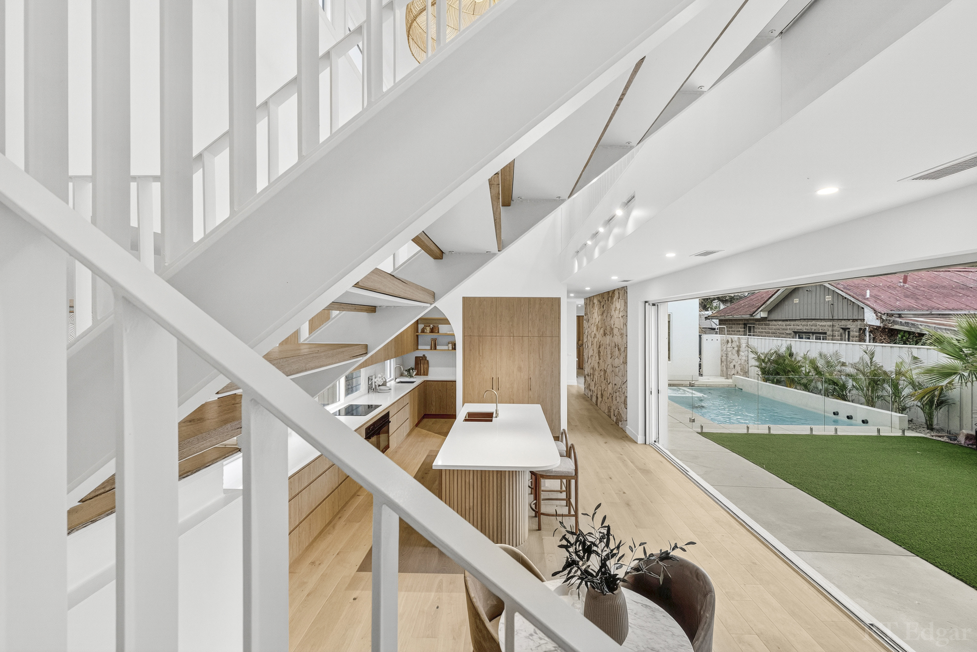 Bright kitchen and living area with an open staircase and views to the garden and pool