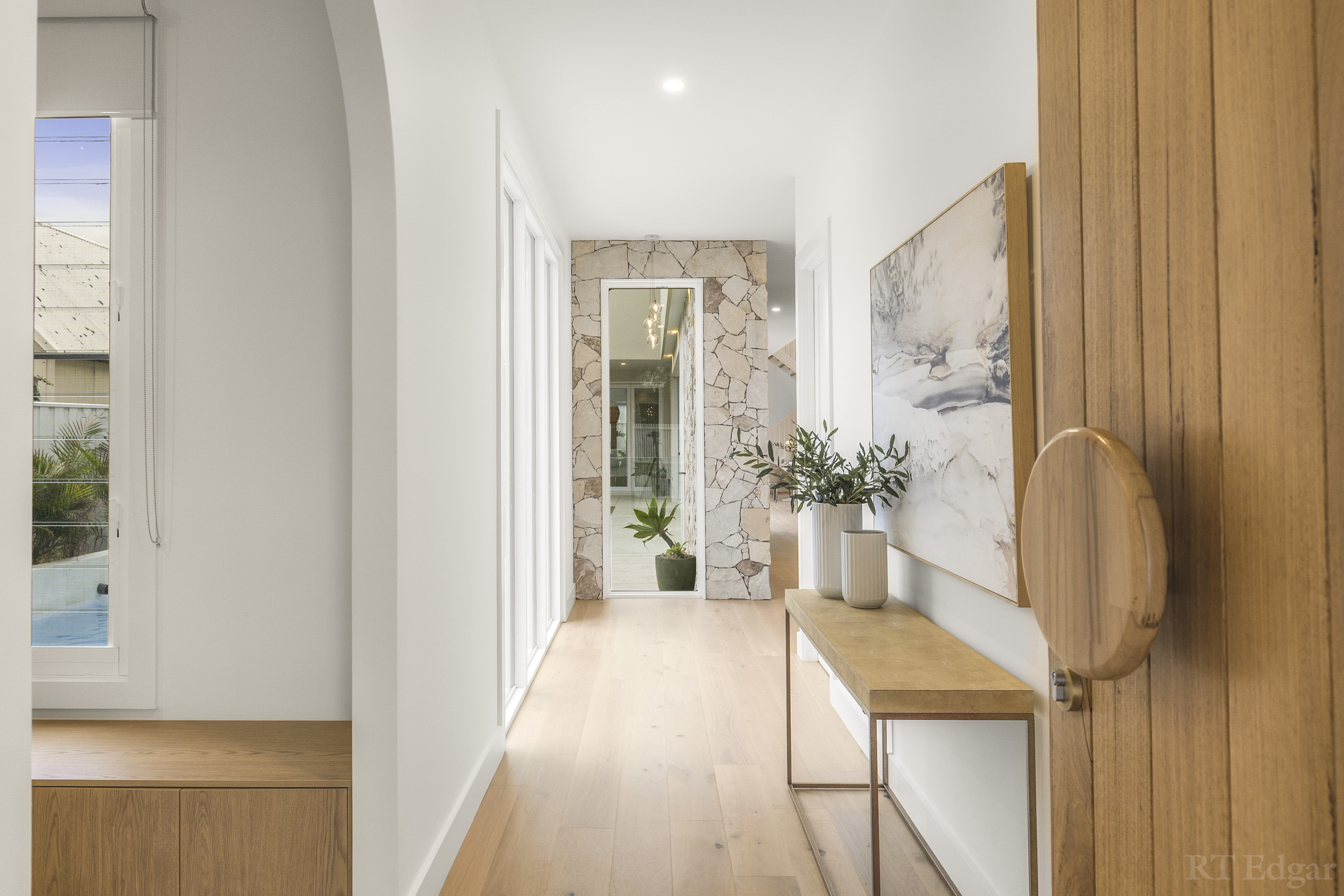 Crafted entry hall with pale timber flooring, a statement pivot door and stone detailing