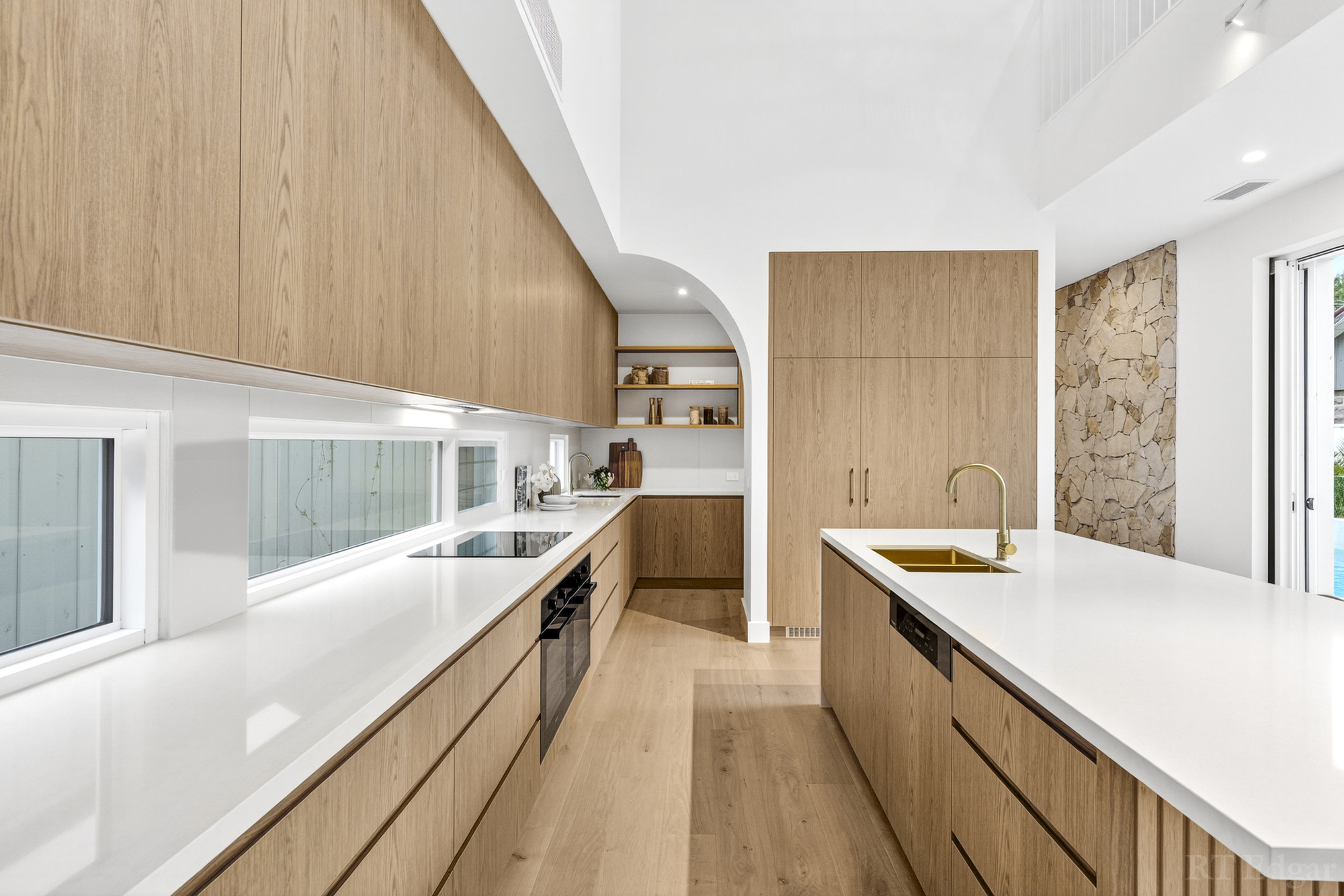 Long galley kitchen with timber cabinetry, white benchtops and stone detailing