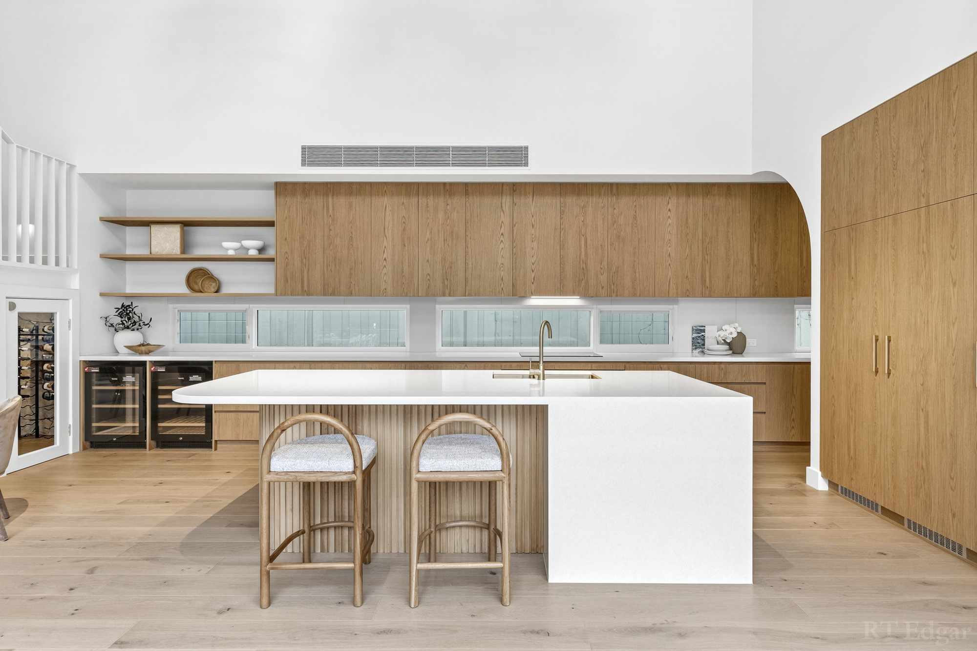 Timber and white kitchen with a large island, cane stools and integrated wine fridges