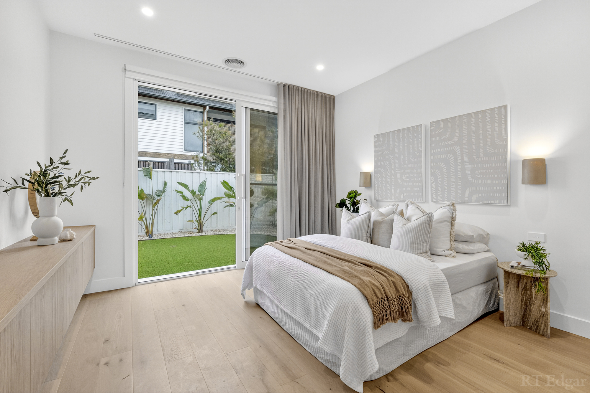 Neutral bedroom opening through glass doors to a landscaped courtyard