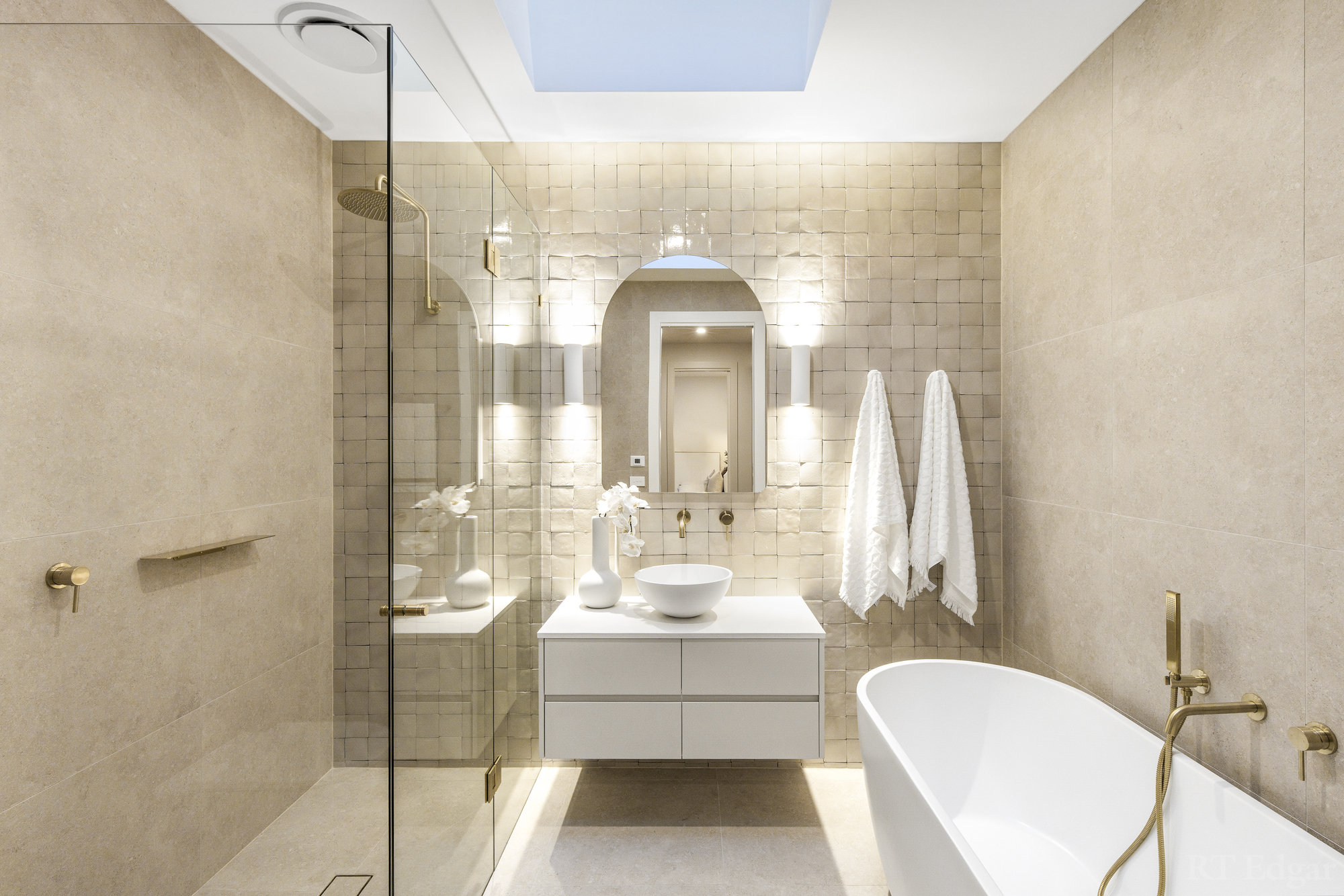 Bathroom finished in stone with a skylight, glass shower, timber vanity and freestanding bath